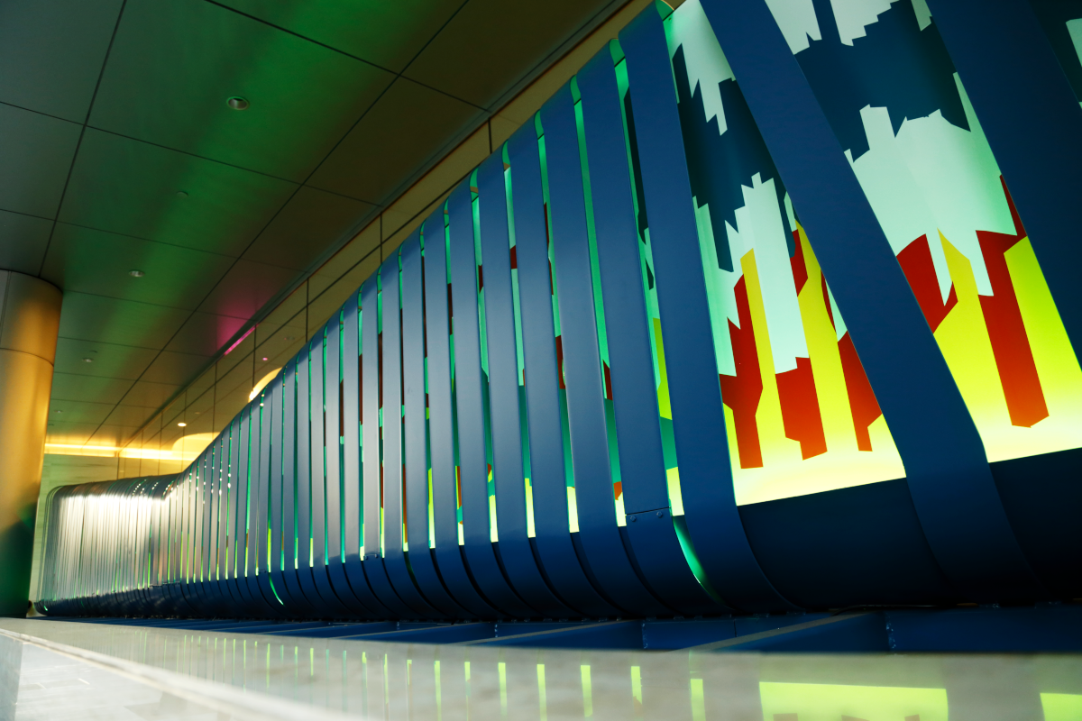 Colorful illuminated modern architectural installation with vertical panels and digital artwork, likely in a public space or art gallery, featuring themes of city skylines and abstract shapes.