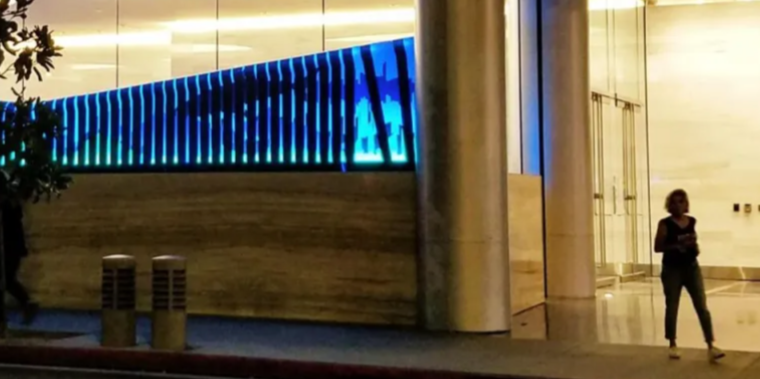 A woman standing outside a modern building with a blue LED light display and glass doors.