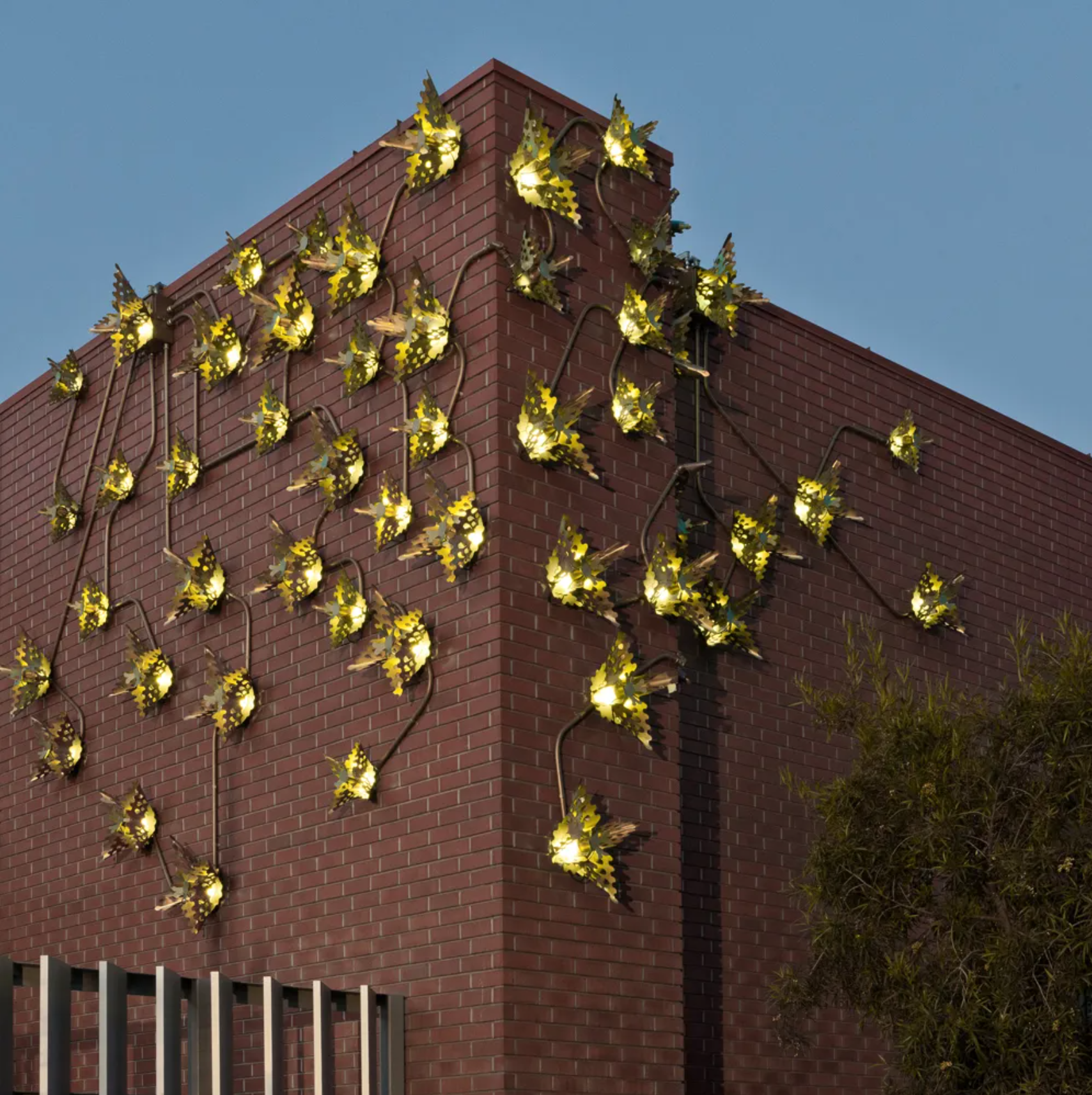 Decorative yellow butterfly-shaped string lights on the corner of a red brick building at dusk