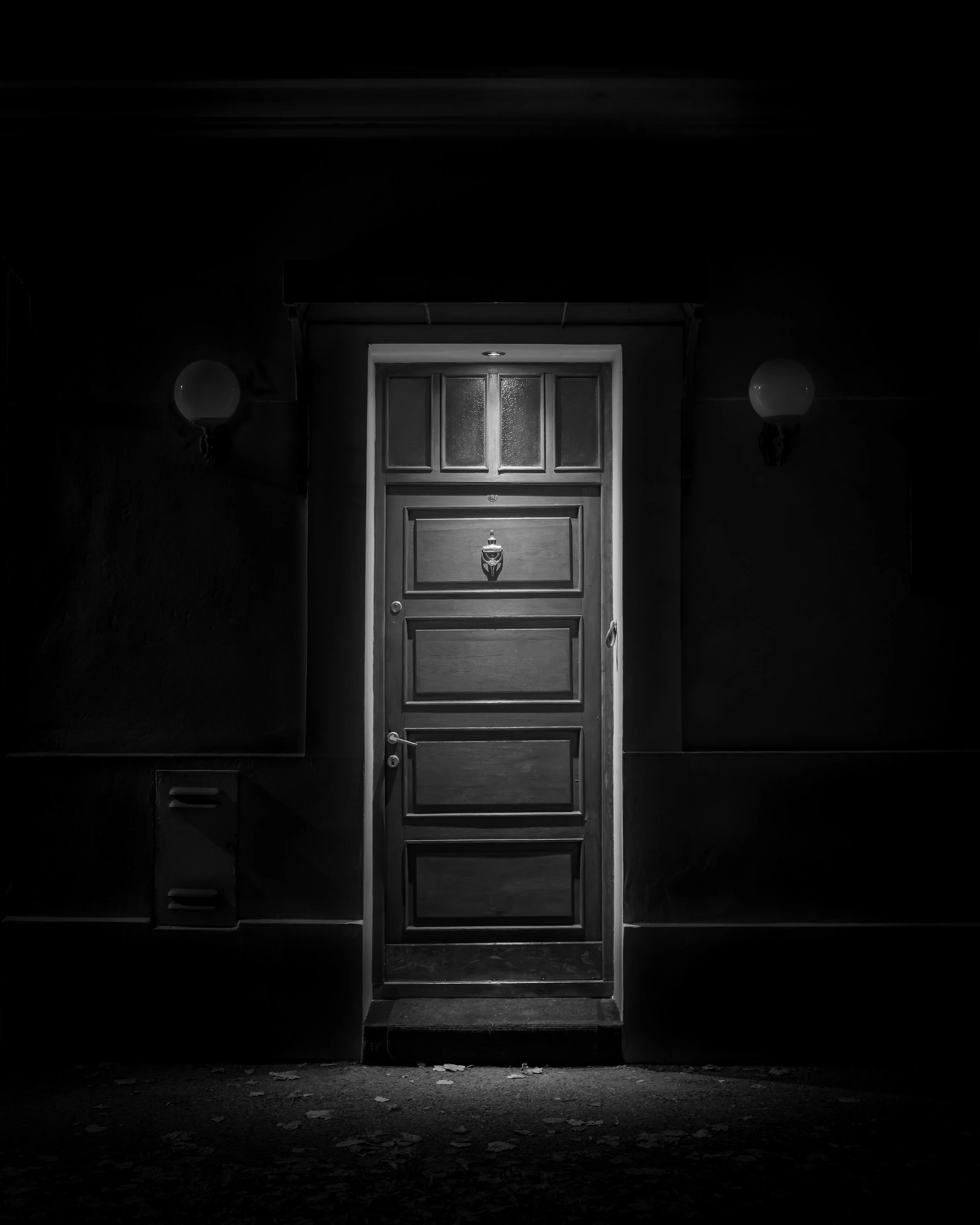 Black-and-white photograph of a solitary illuminated doorway surrounded by deep shadow.