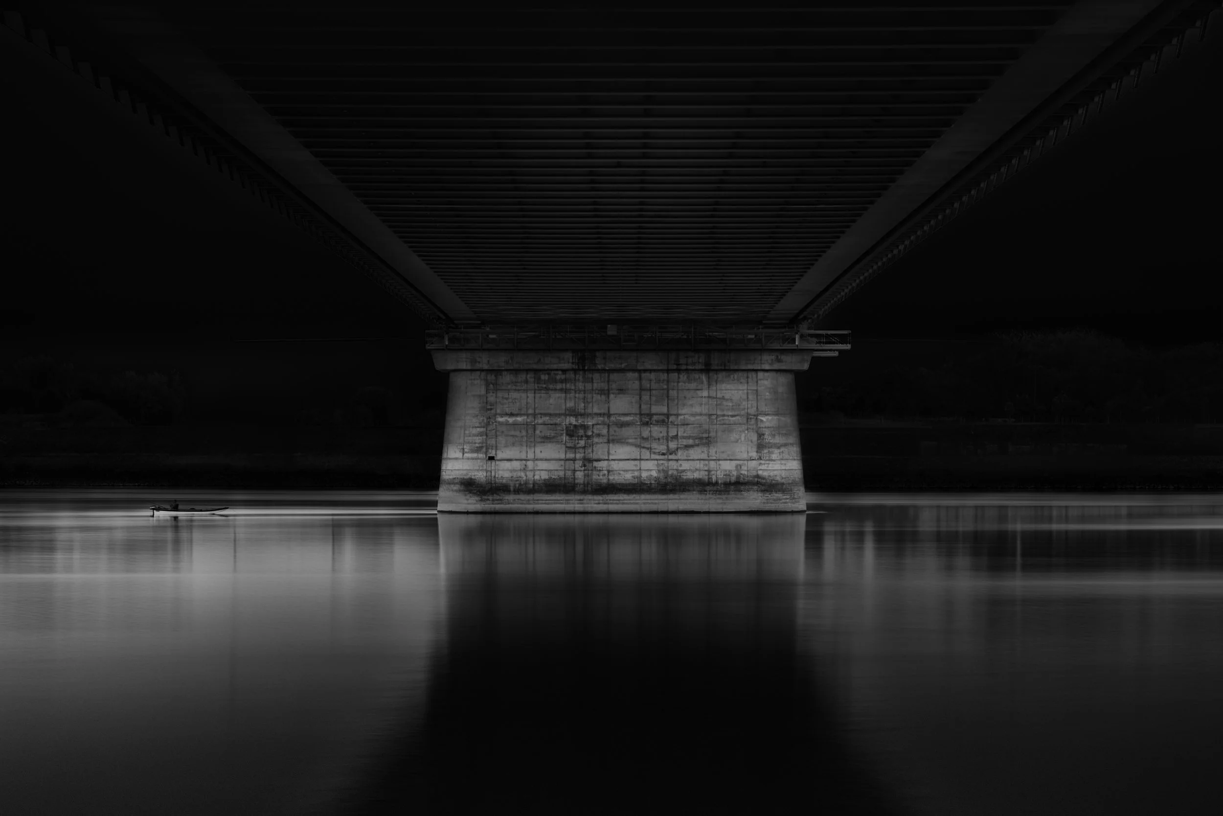 Black-and-white photograph of a bridge and a small boat reflected in still water