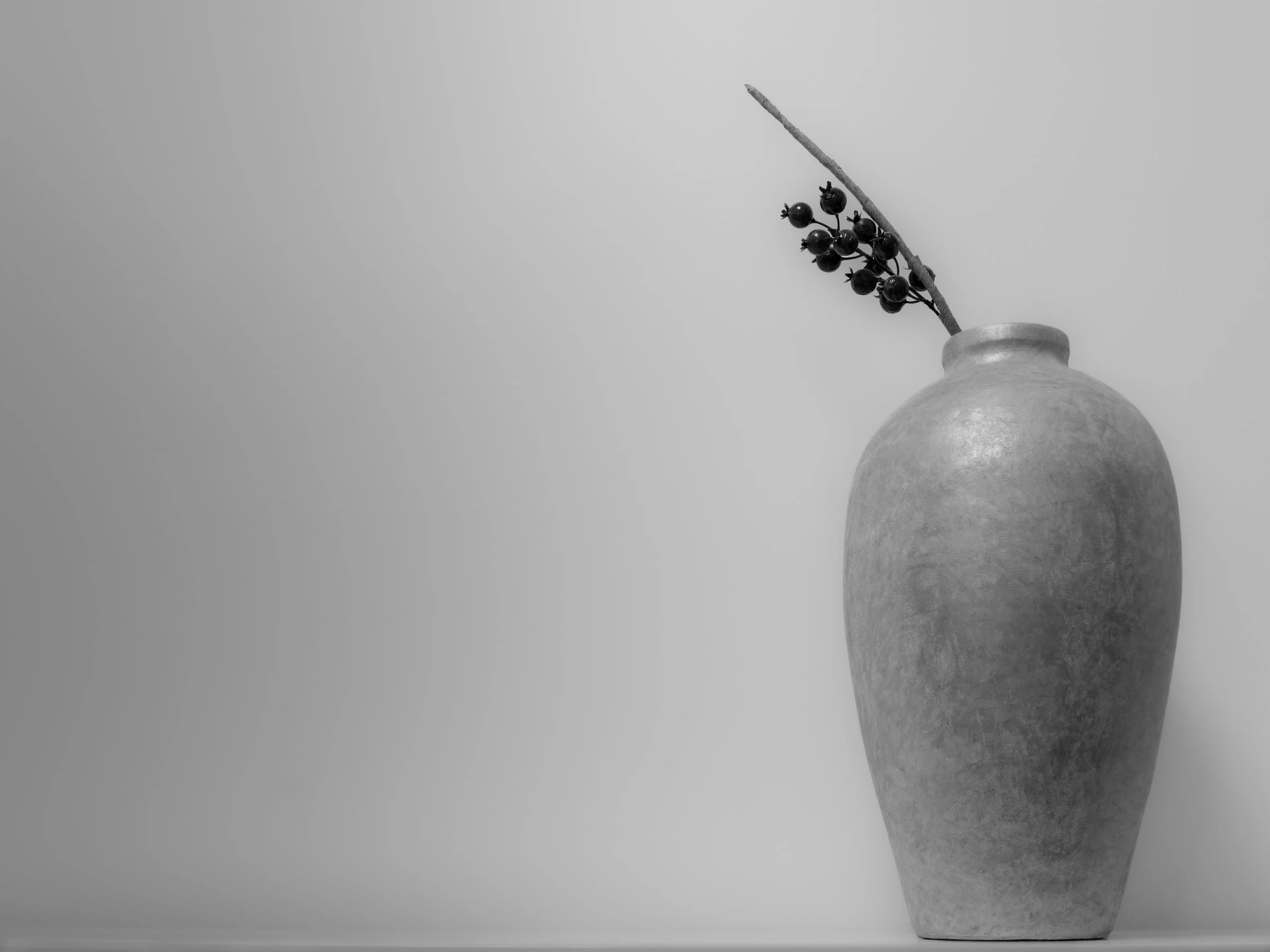 Black-and-white still life of a tall vase with a flowering branch