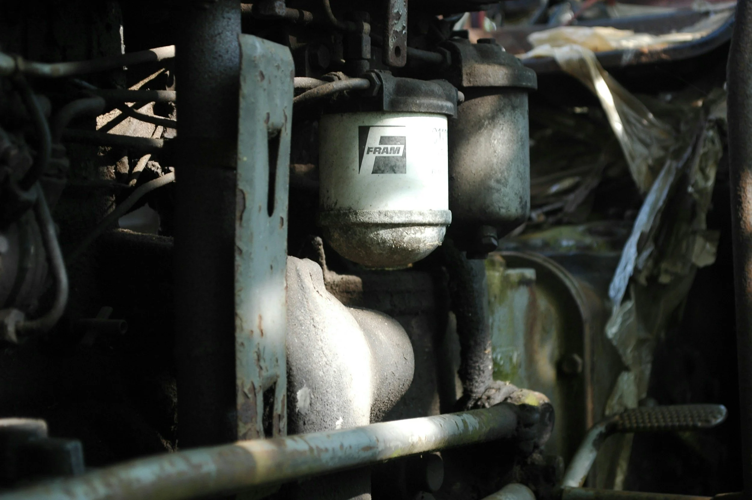 Close-up of a dirty, weathered automotive fuel filter marked with the brand 'FRAM', installed in a vehicle engine bay.