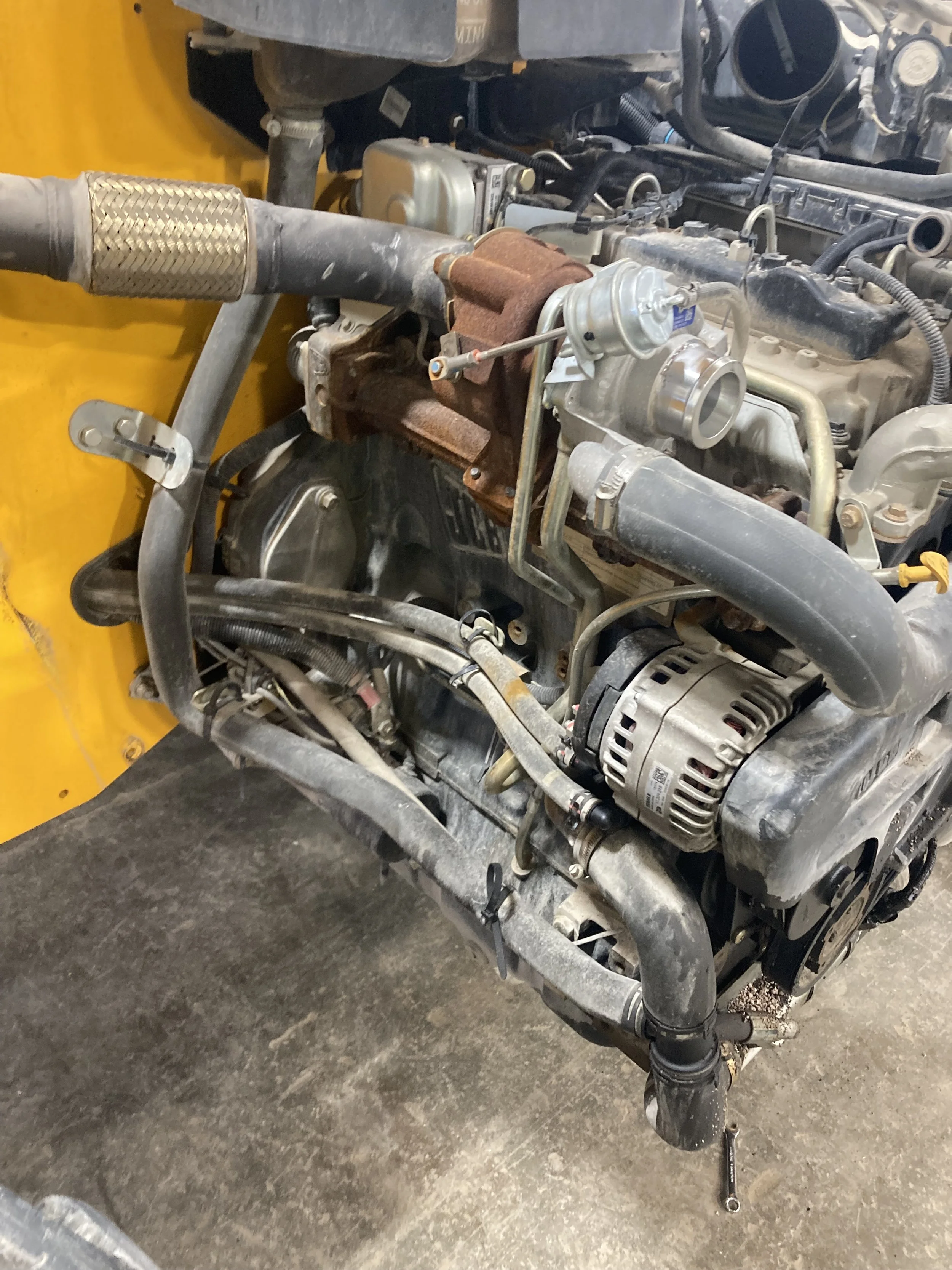 A close-up view of a vehicle engine with various mechanical parts, hoses, and a rusty component.