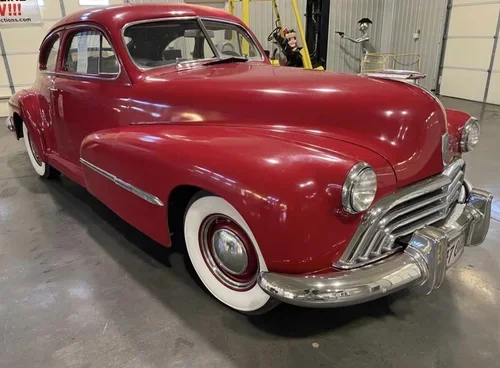 Red vintage classic car with whitewall tires parked indoors.