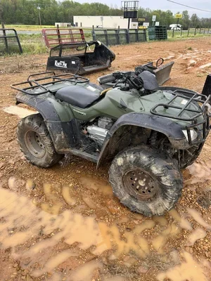 A green all-terrain vehicle (ATV) covered in mud, parked on a muddy trail.
