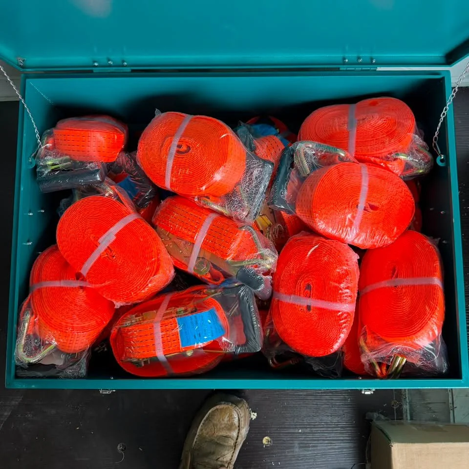 A teal metal box filled with individually wrapped orange extension cords or electrical cables.