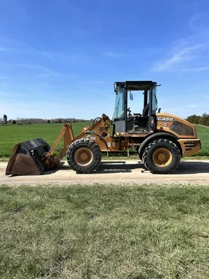 A construction loader parked on a dirt path with green grass and a blue sky with some clouds in the background.