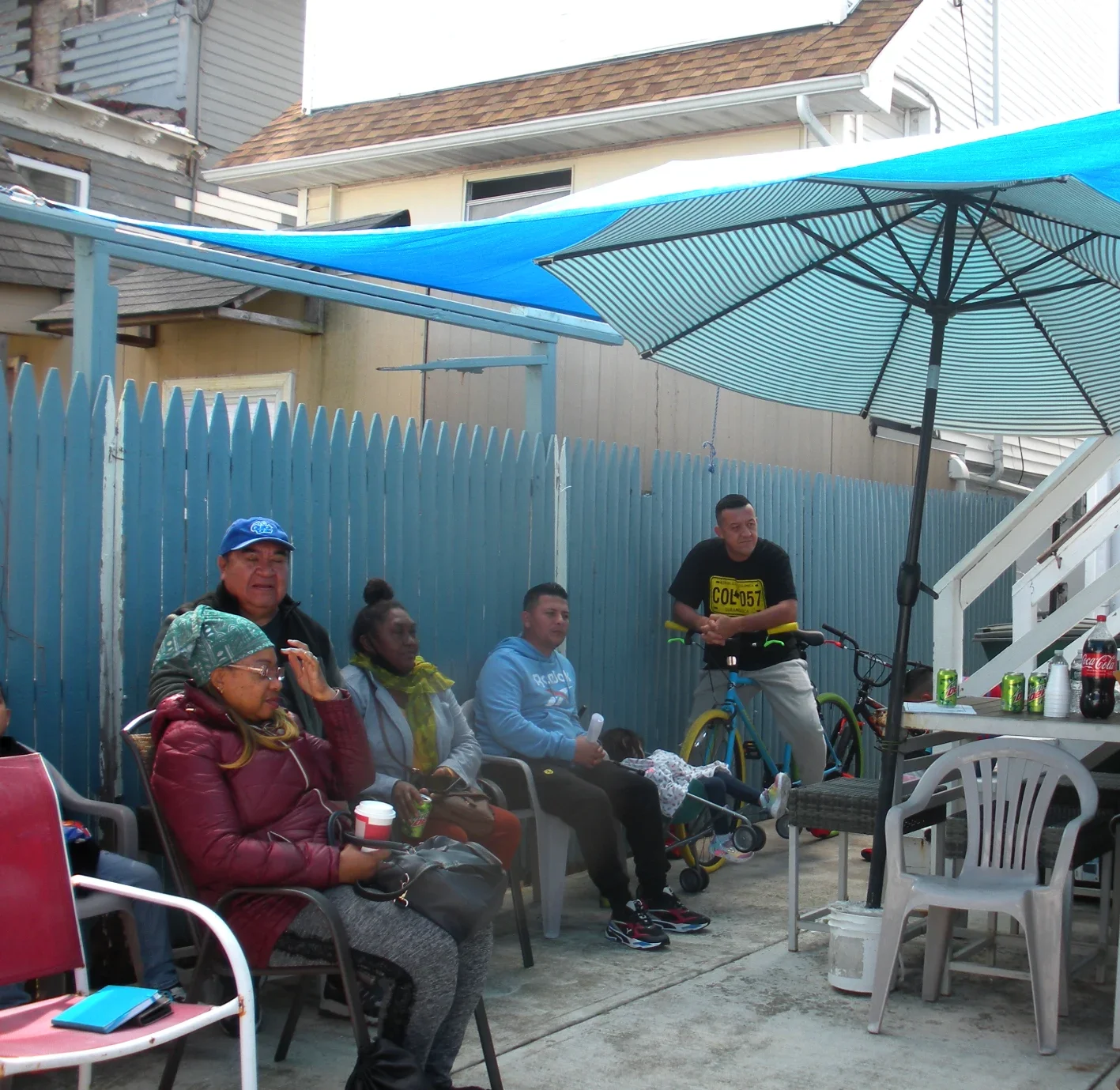 Five people gather in a yard with an umbrella