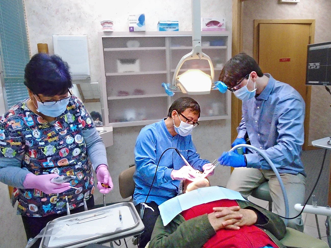 A dentist next to two dental assistants work on a patient