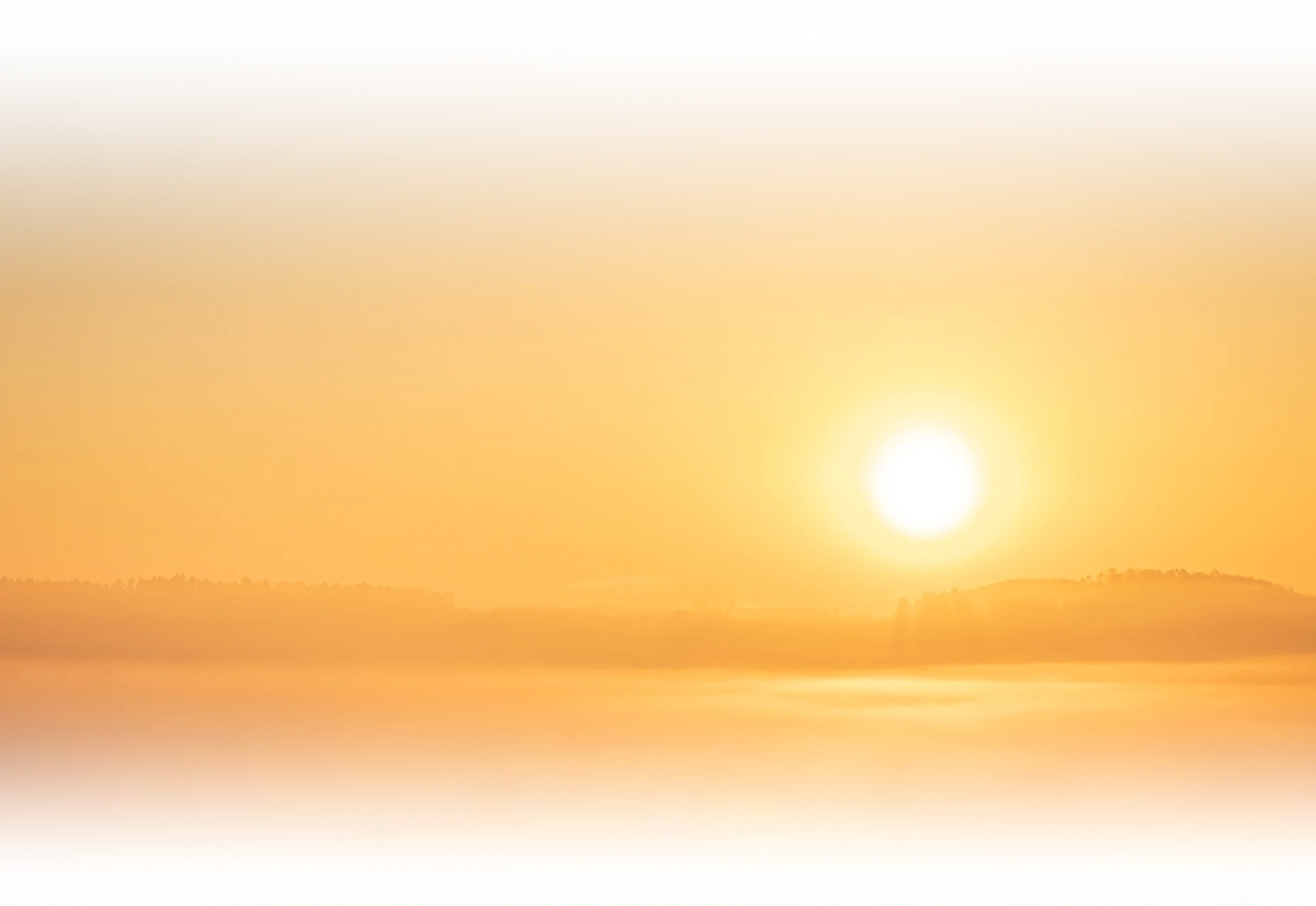 A sunset or sunrise over a landscape with the sun partially visible near the horizon and distant trees or fields.