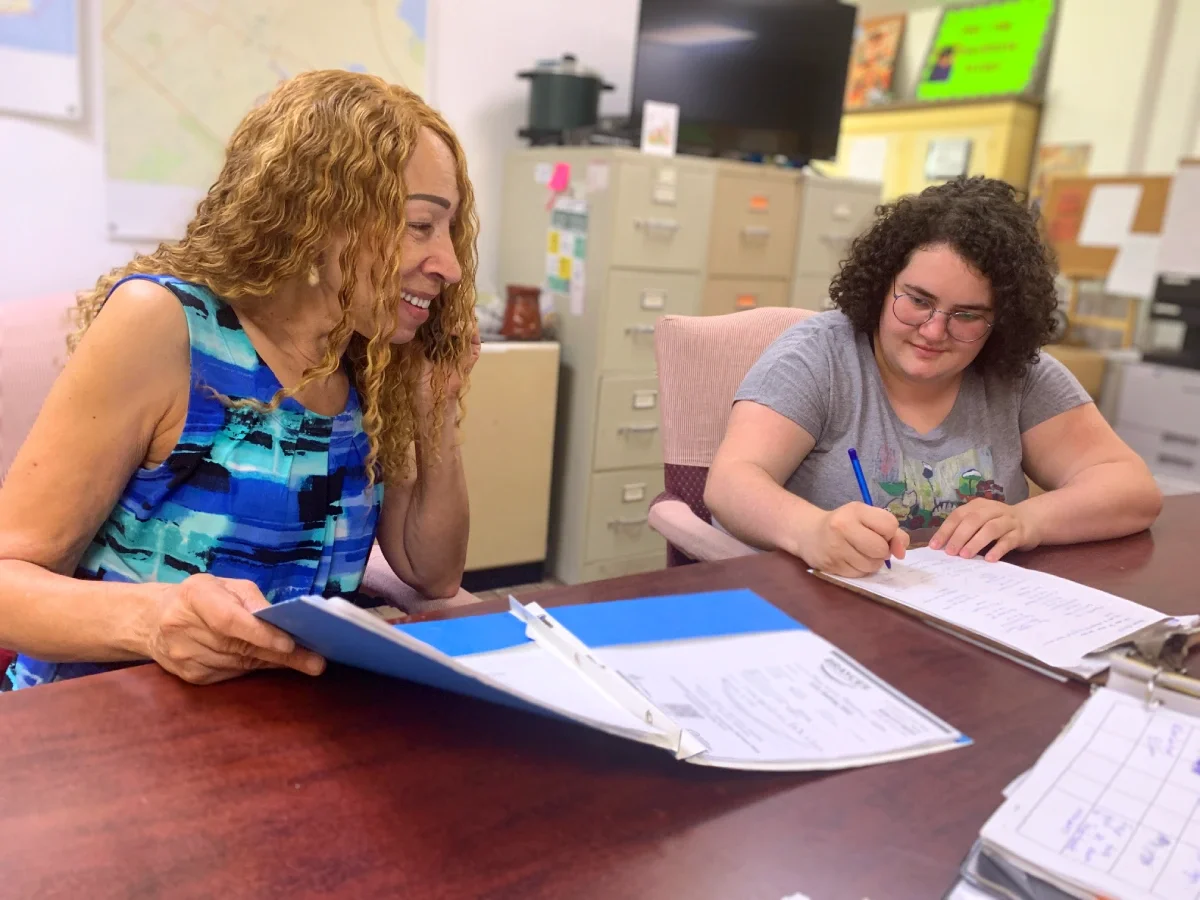 A woman making a phone call and looking at a folder as another woman takes notes