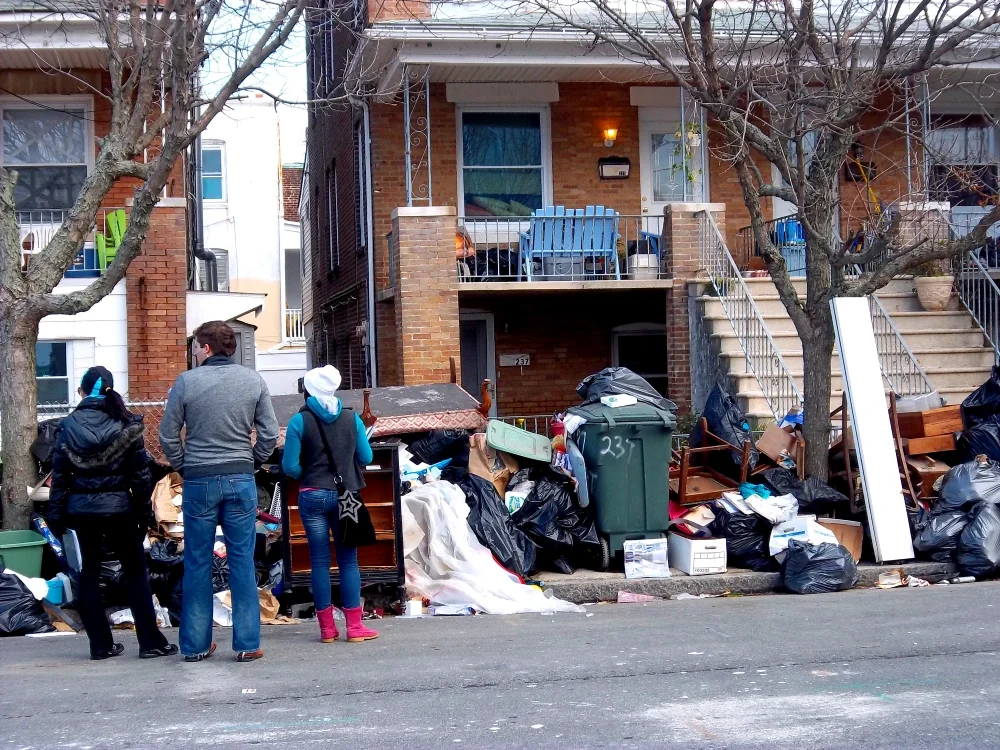 Three volunteers take notes while looking at piles of garbage outside of two homes