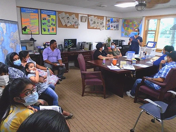 A dentist speaks to a group while a child looks at the camera