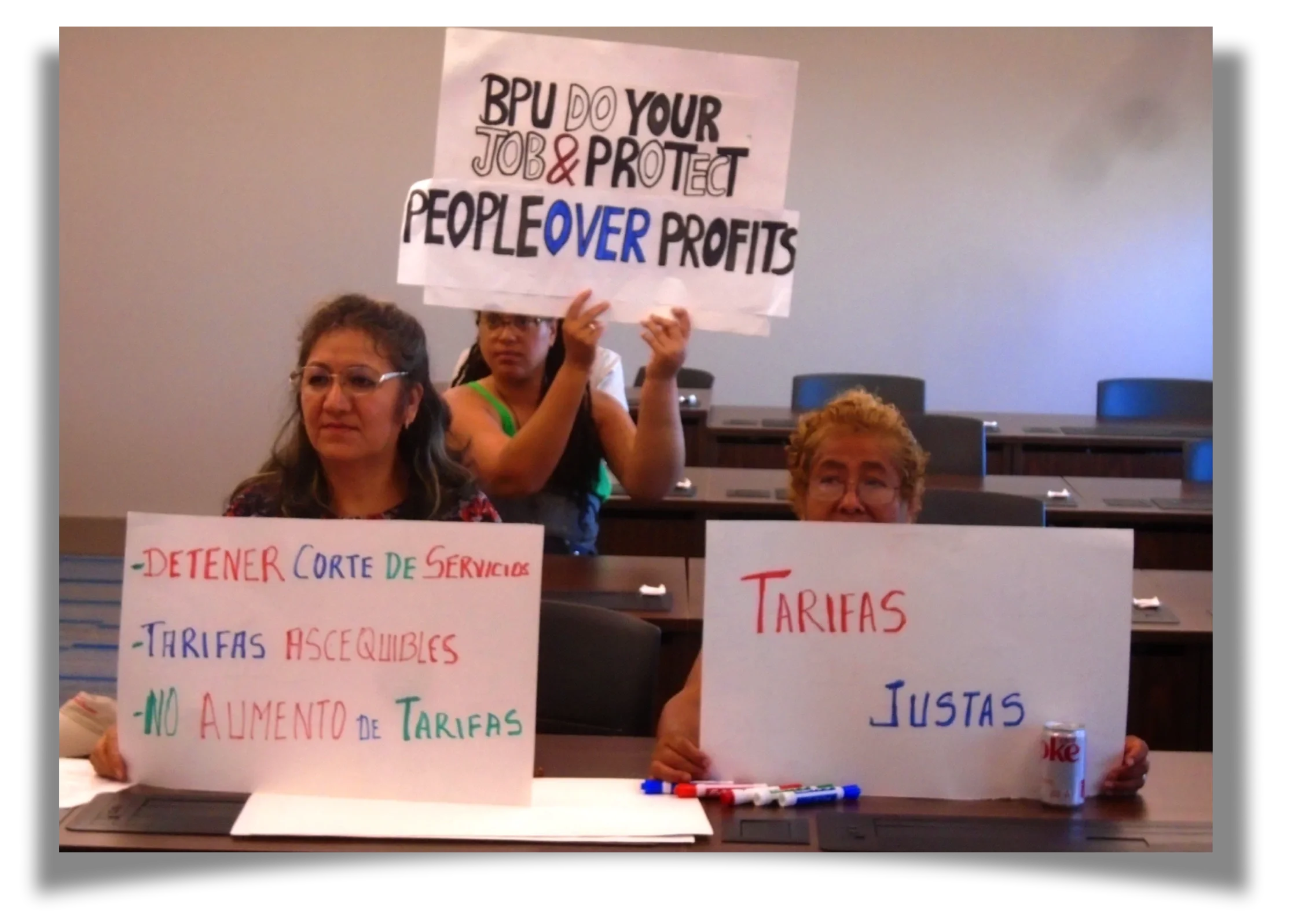 Three women hold signs which read "BPU Do Your Job & Protect People Over Profits," "Tarifas Justas" and "Tarifas Ascequibles"