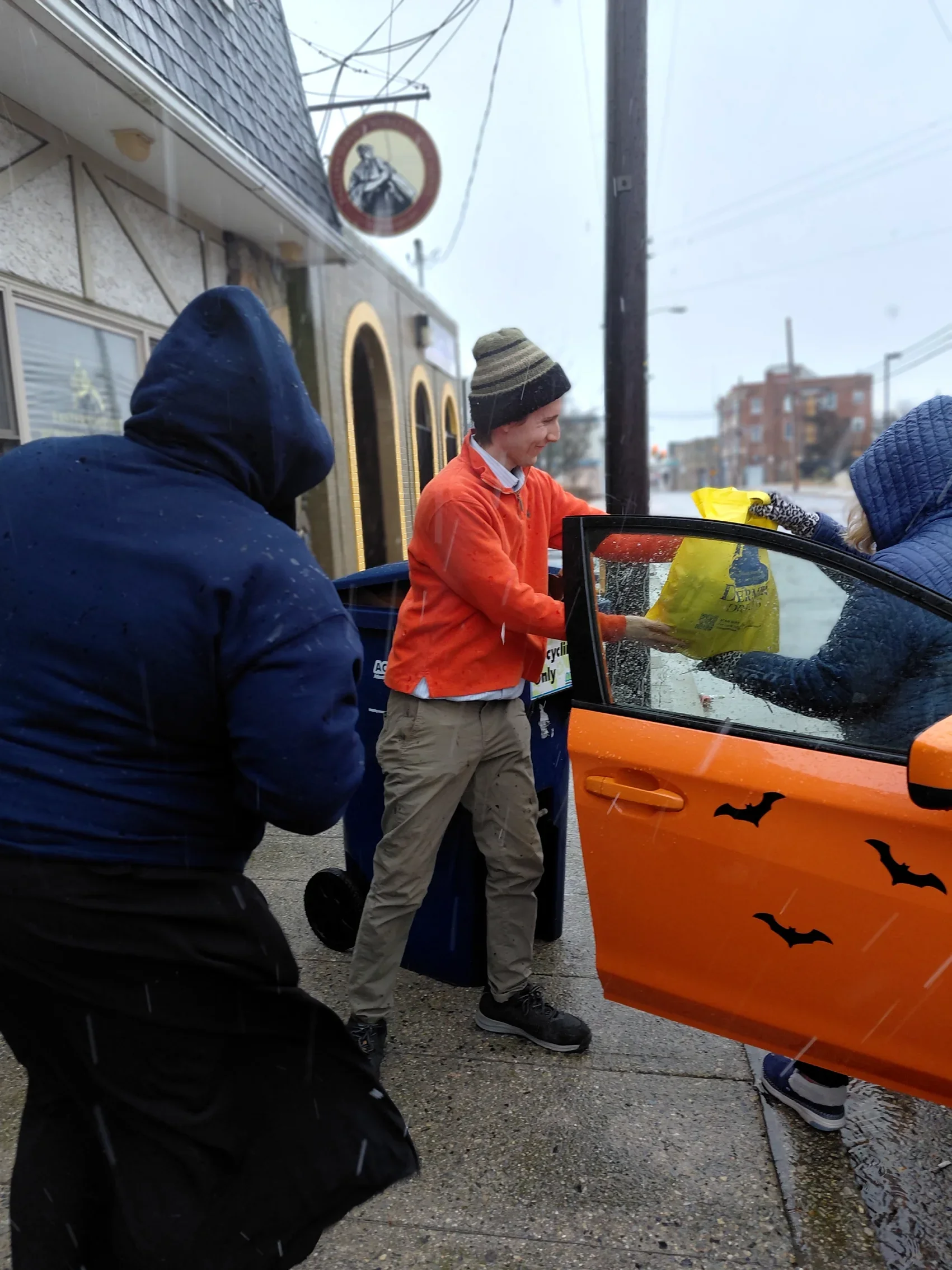 In the sleet, a man with a hat hands a bag of food to a woman