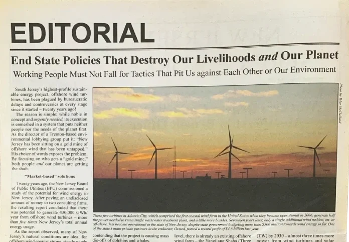 A photo of a sunset with windmills printed on a newspaper whose caption reads "End State Policies That Destroy Our Livelihoods and Our Planet"