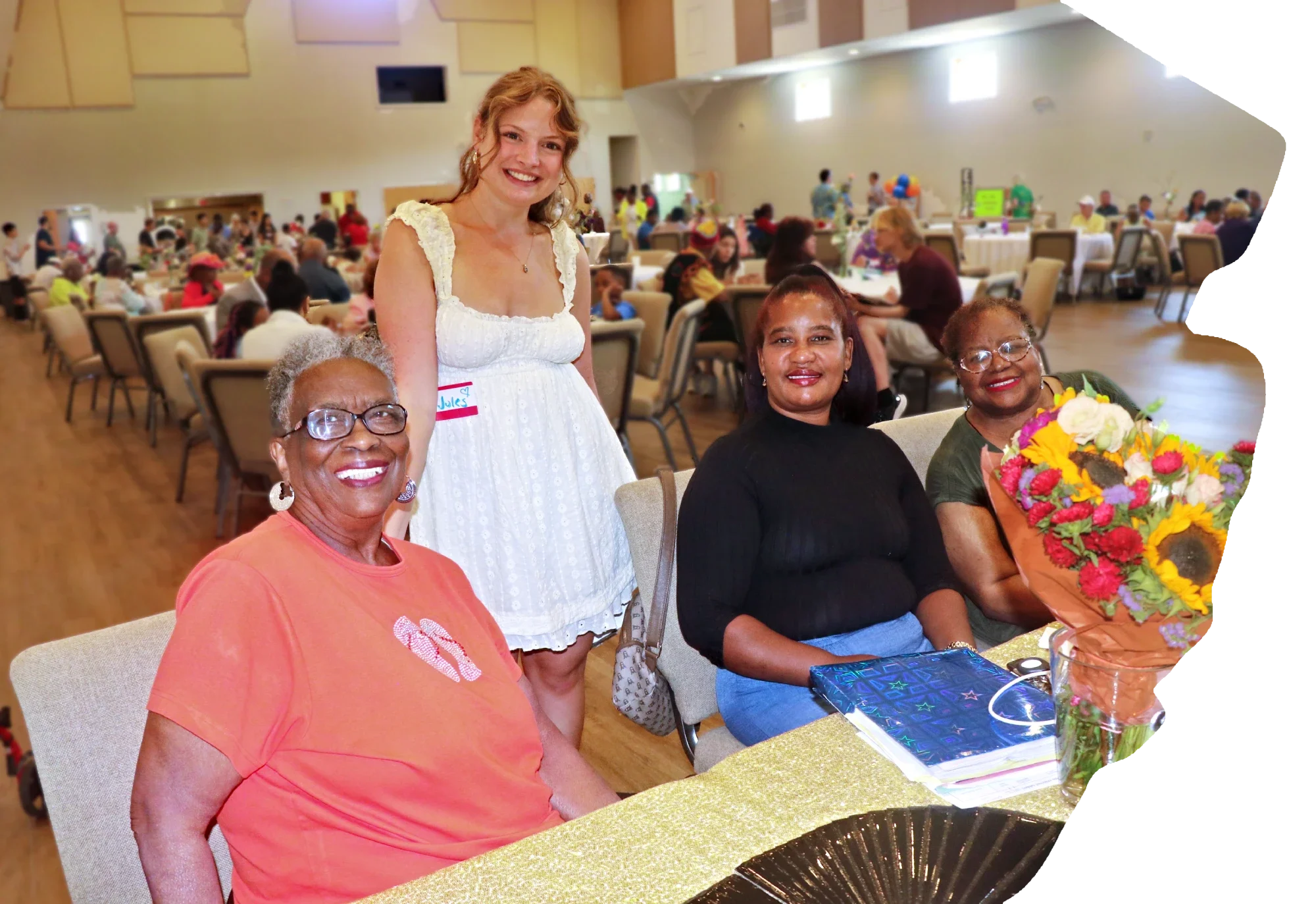Four people behind a table smile with a bouquet of flowers