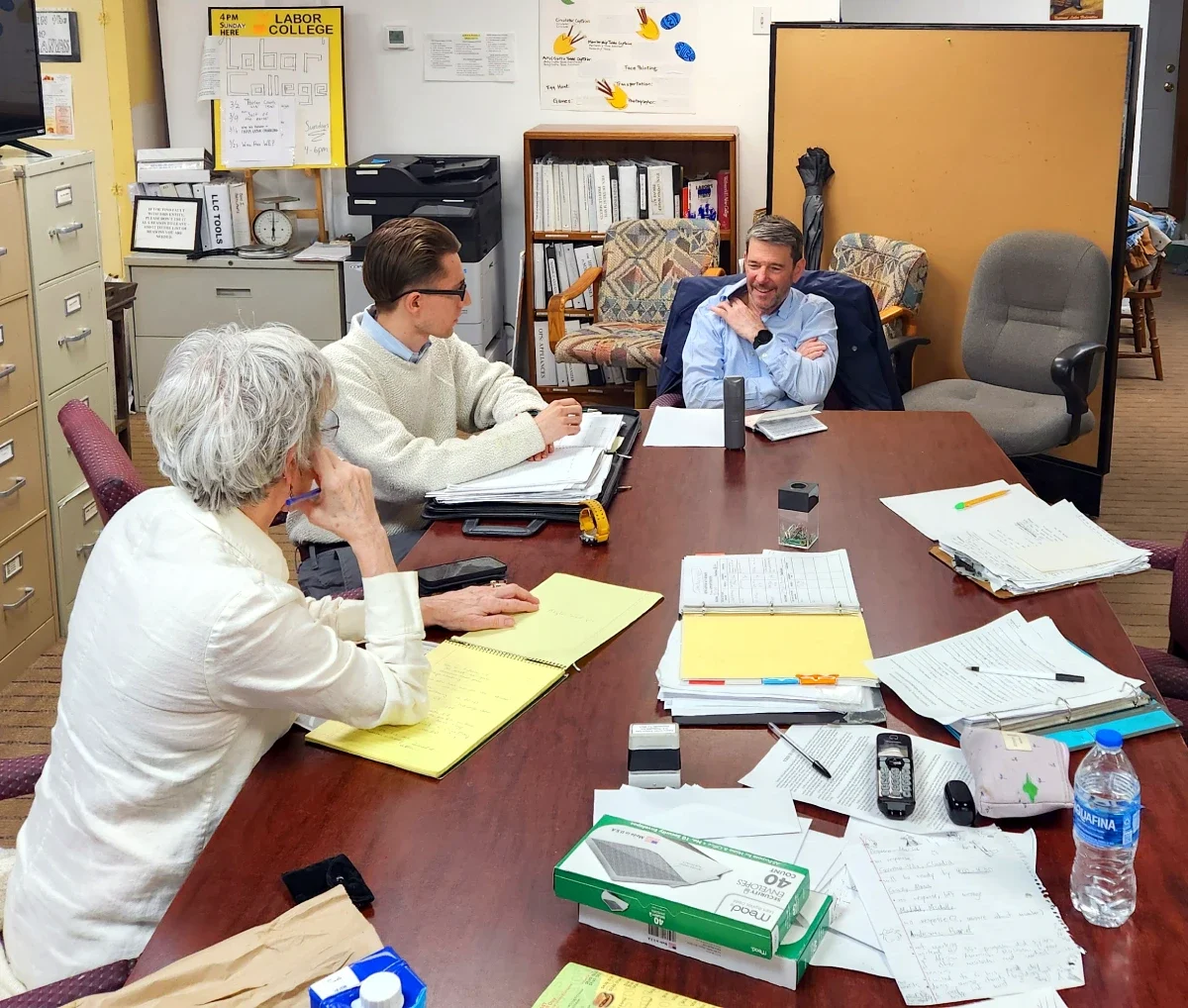 A lawyer at the head of a table speaks while two volunteers listen
