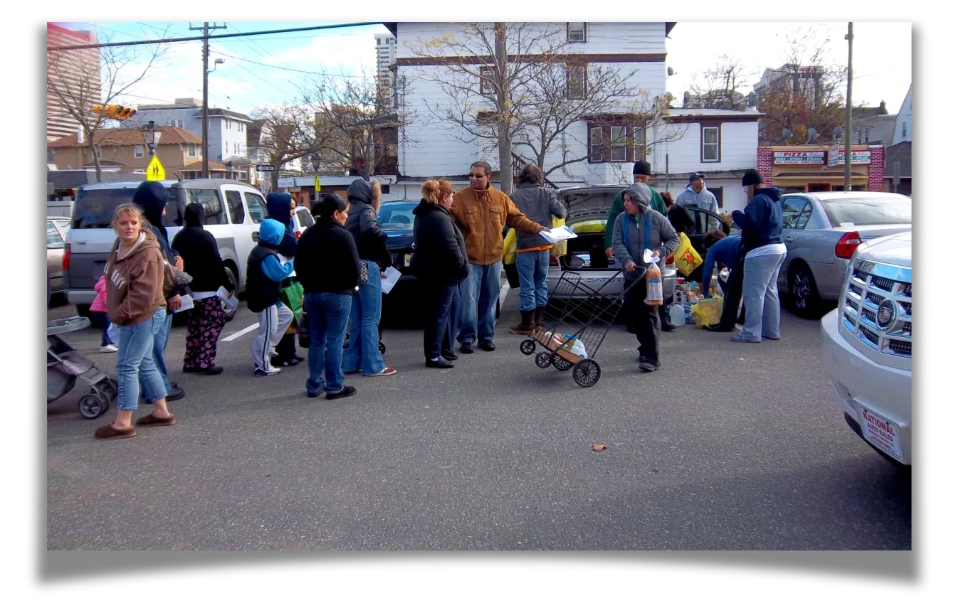 A line of people behind a parked car with volunteers distributing supplies