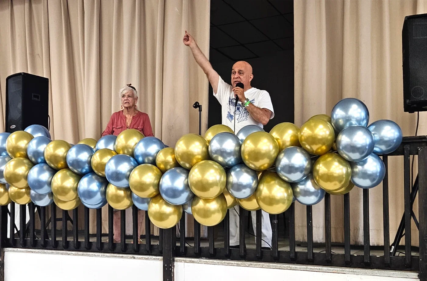 On stage decorated with blue and gold ballons, a man and woman speak
