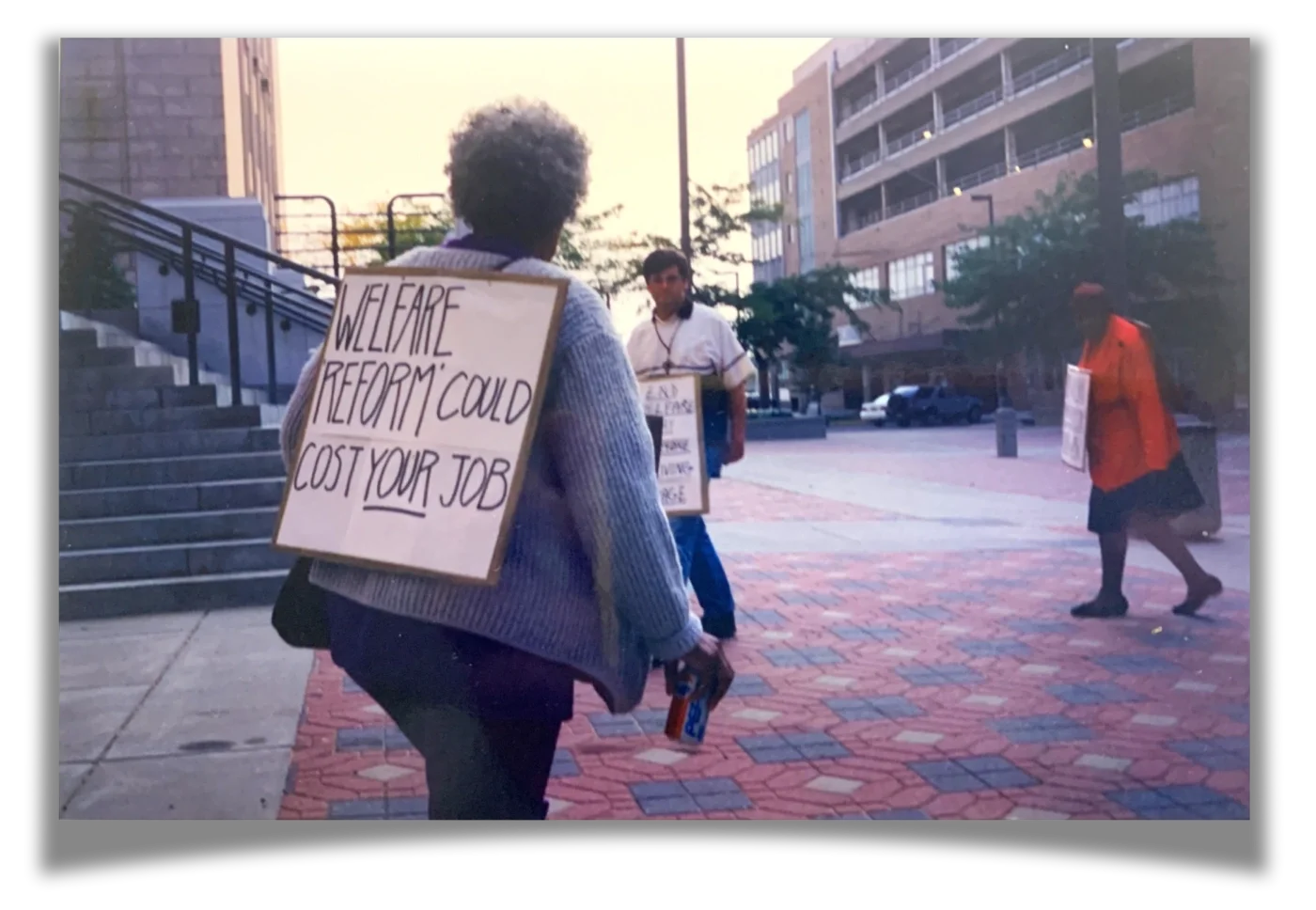 A woman walking with a sign over her shoulders that reads "Welfare reform could cost your job"