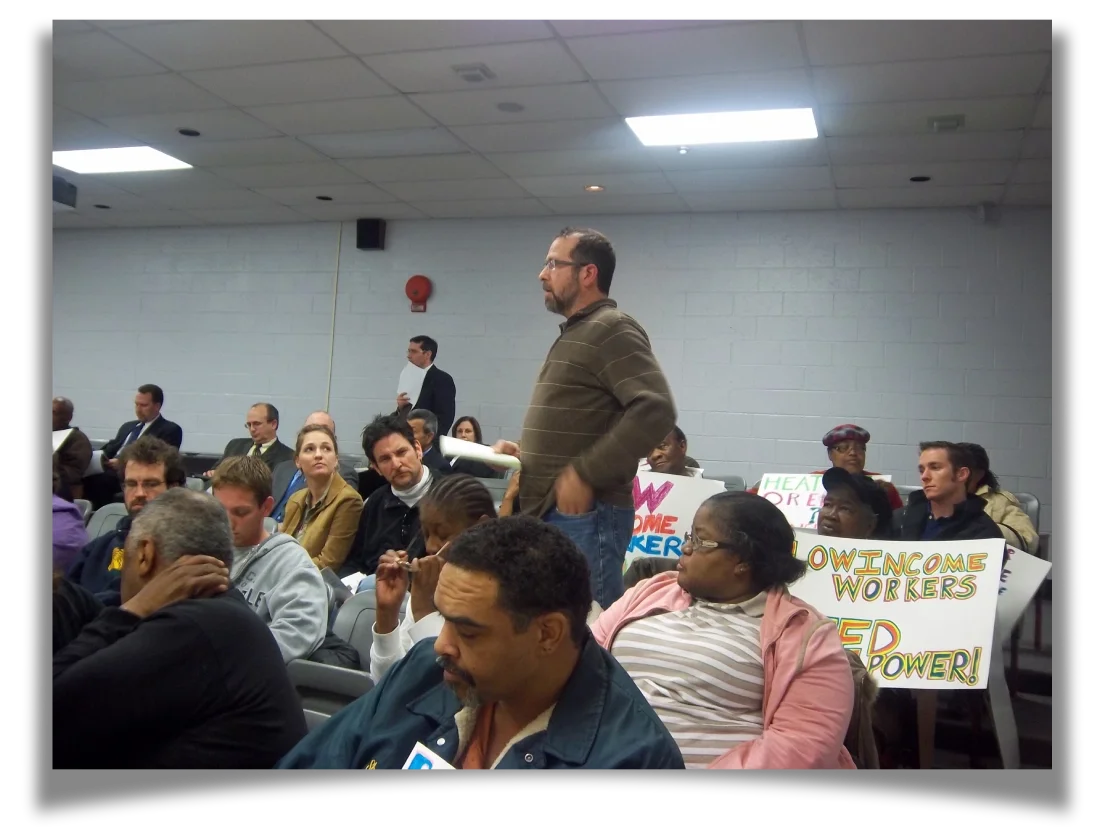 14.	A man testifies while standing amidst a crowd of people with signs