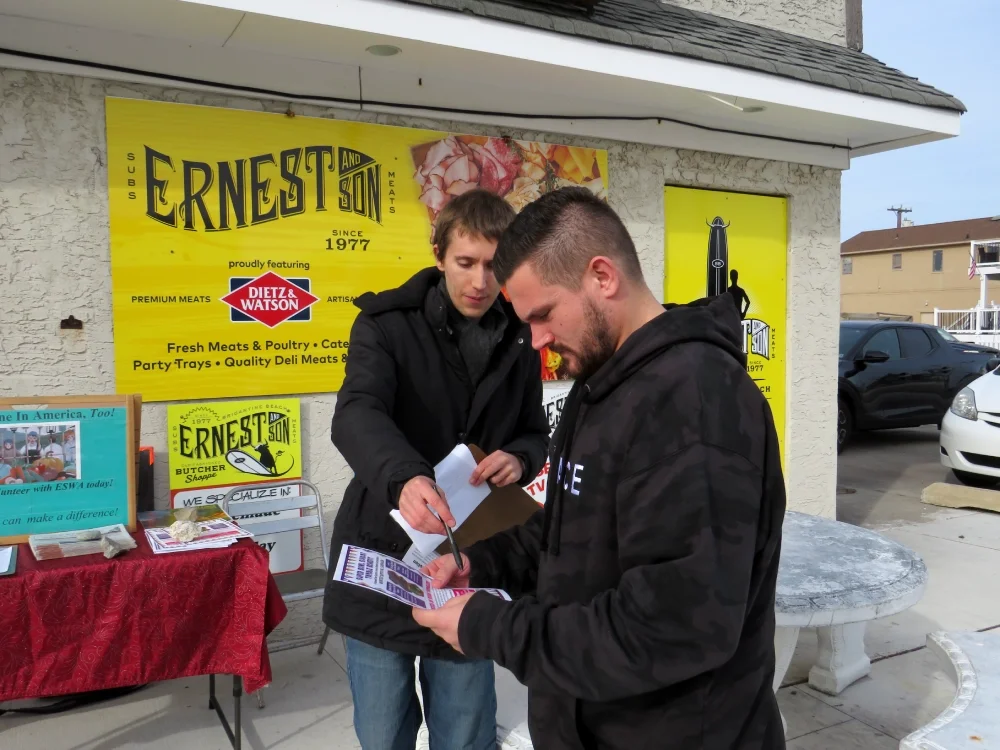 A man reads a flyer an ESWA volunteer points out an image on the flyer