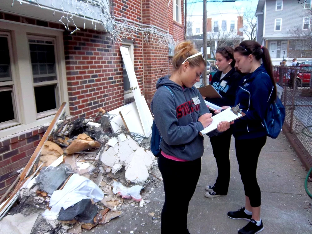 Three volunteers take notes outside a building with a pile of debris