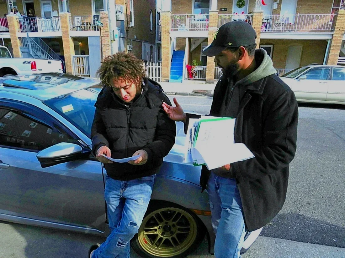 A man speaks to another man next to row homes.