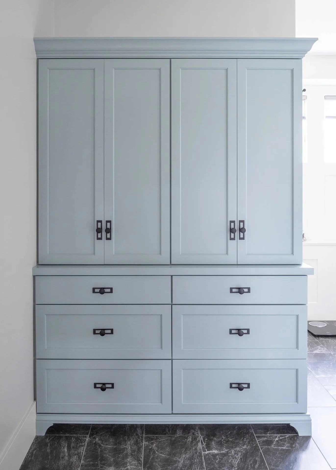 A light blue, tall, custom cabinet with multiple drawers and doors, situated against a white wall, on a dark, marbled tile floor.