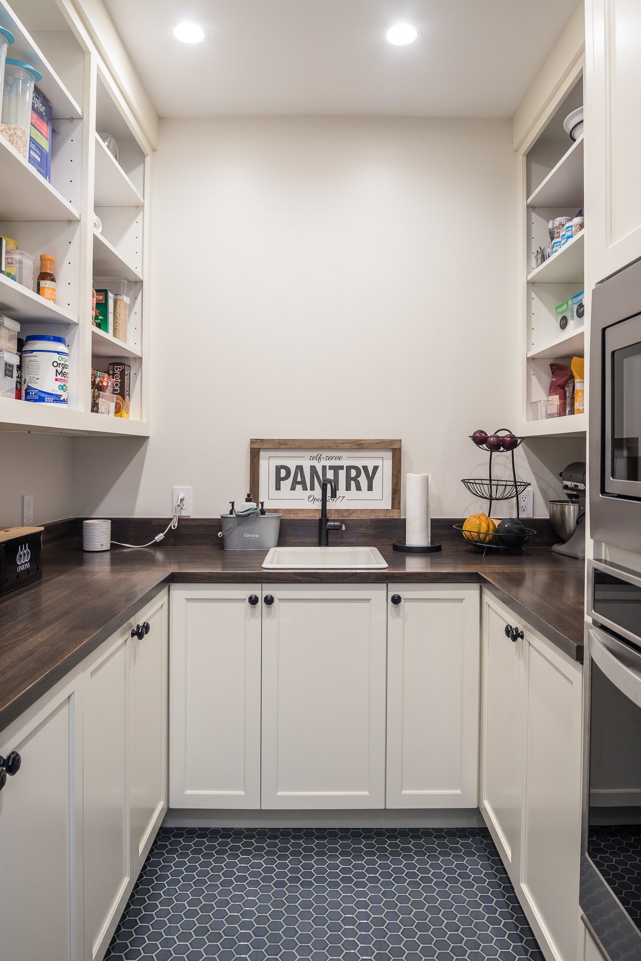 Walk-in pantry with white custom cabinets, dark countertops, and open shelving