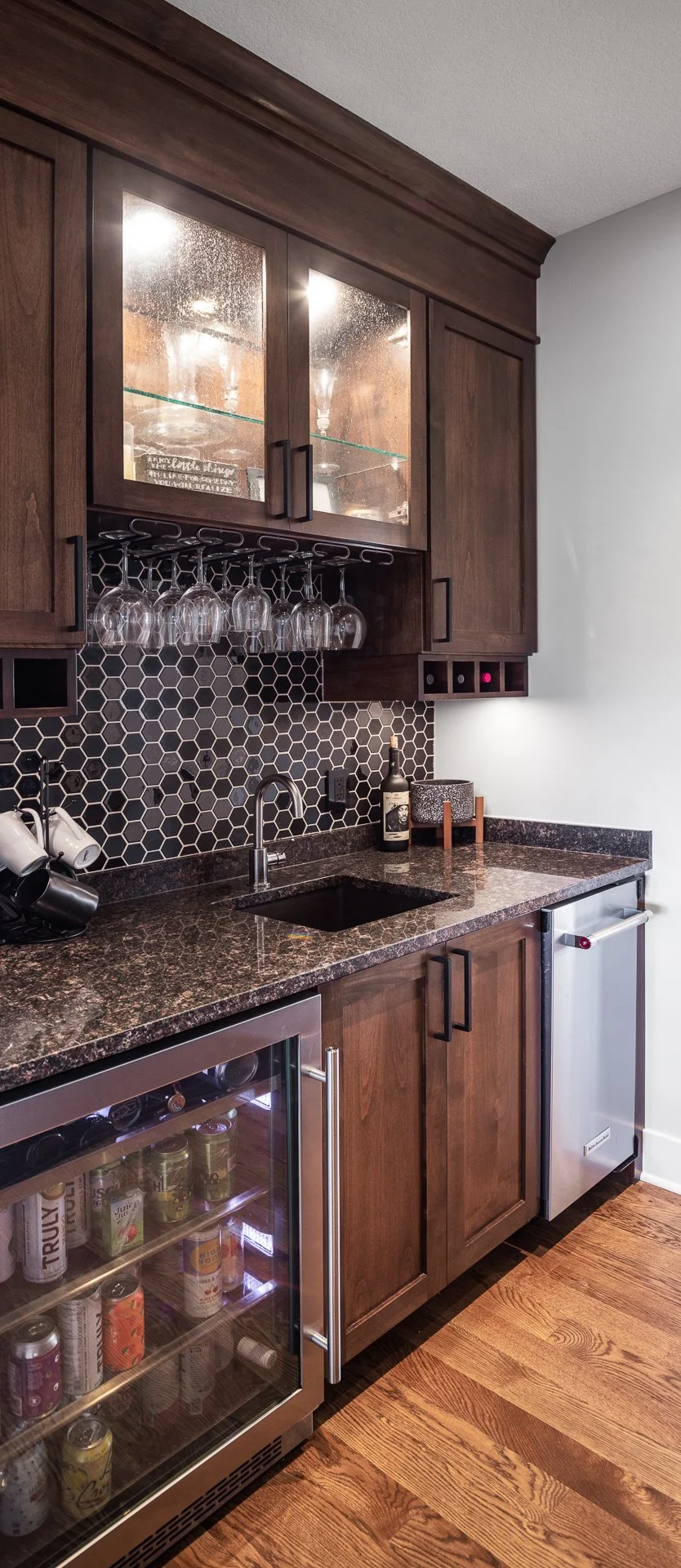 Dark wood custom cabinetry with built-in wine glass storage, tile backsplash, and granite countertop