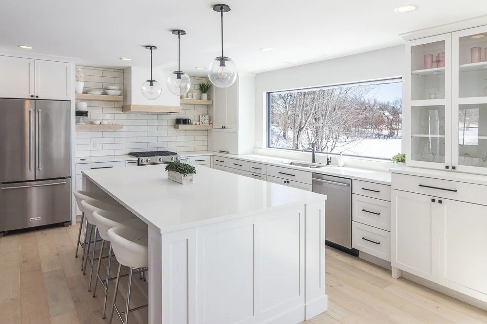 Plymouth, MN custom kitchen remodel. White modern kitchen, huge windows looking out over Schmidt Lake. black hardware on white cabinets. modern hood vent with wood detailing.
