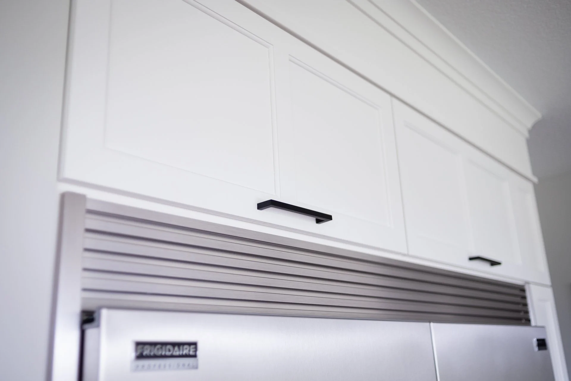 White custom upper cabinet with black hardware above refrigerator
