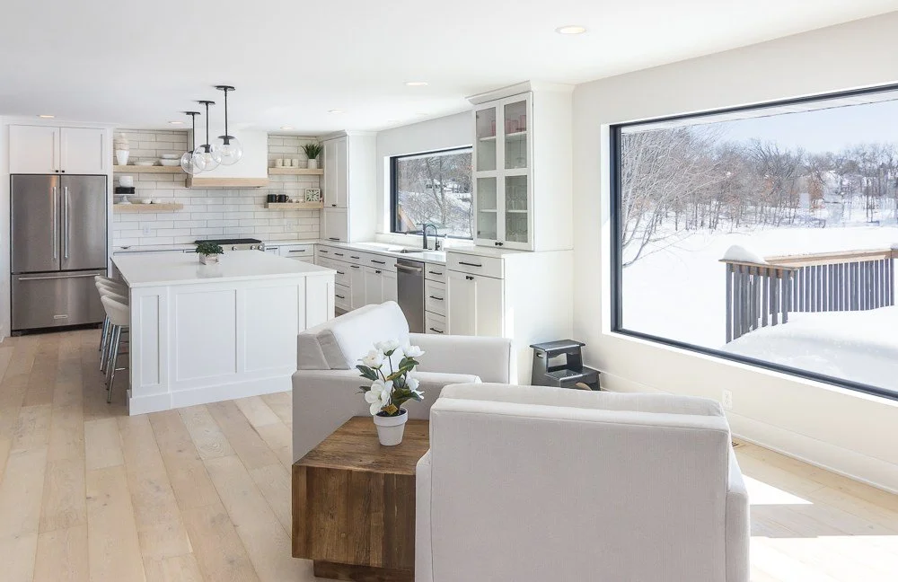 Plymouth, MN custom kitchen remodel. White modern kitchen, huge windows looking out over Schmidt Lake. black hardware on white cabinets. modern hood vent with wood detailing. sitting area overlooking lake.