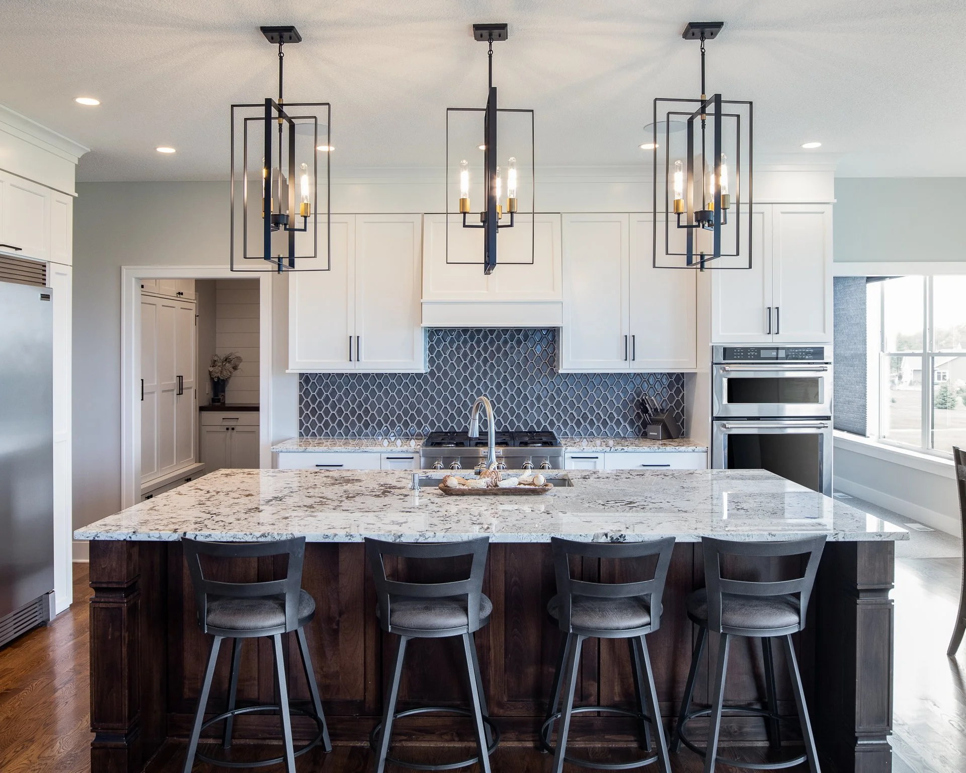 Custom white kitchen cabinetry with large island, granite countertops, and geometric pendant lights
