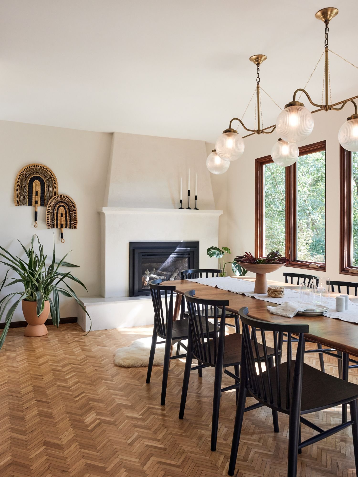 Golden Valley dining room, plaster custom fireplace, gas fireplace, black wood chairs, round glass ball shaped chandelier, terracotta plant, macrame wall hanging. 