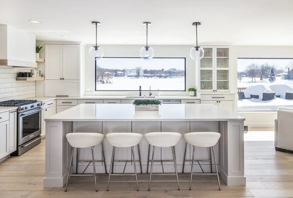 Plymouth, MN custom kitchen remodel. White modern kitchen, huge windows looking out over Schmidt Lake. black hardware on white cabinets. modern hood vent with wood detailing. barstools looking out over the lake.