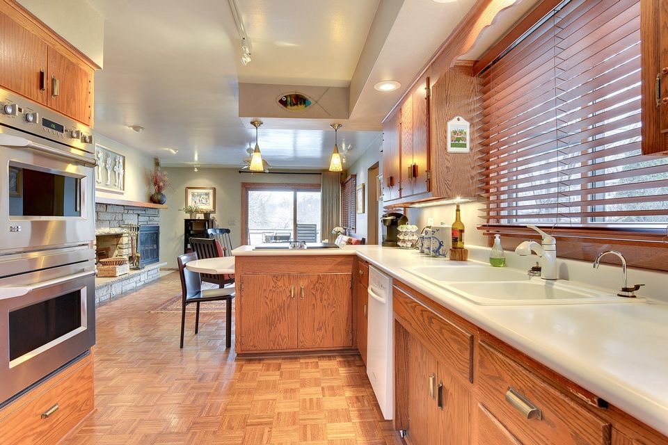 original Edina kitchen, with dated wood cabinets, soffit, much darker and less open. wood blinds, stone fireplace.