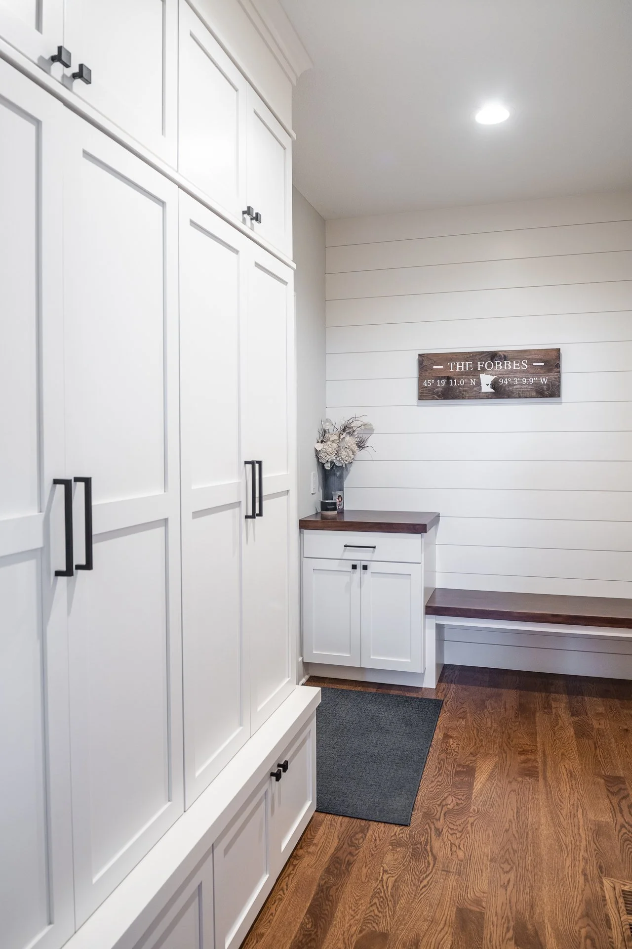 Floor-to-ceiling white custom storage cabinets with black hardware and built-in bench
