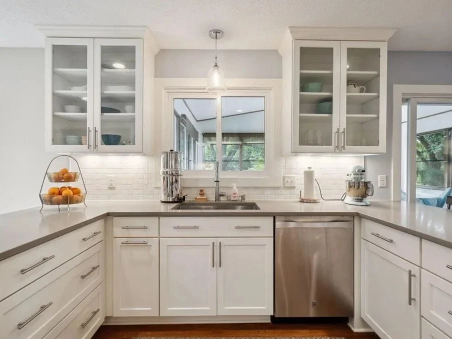 Modern kitchen with white cabinets, glass-front upper cabinets, stainless steel dishwasher, and countertop appliances.