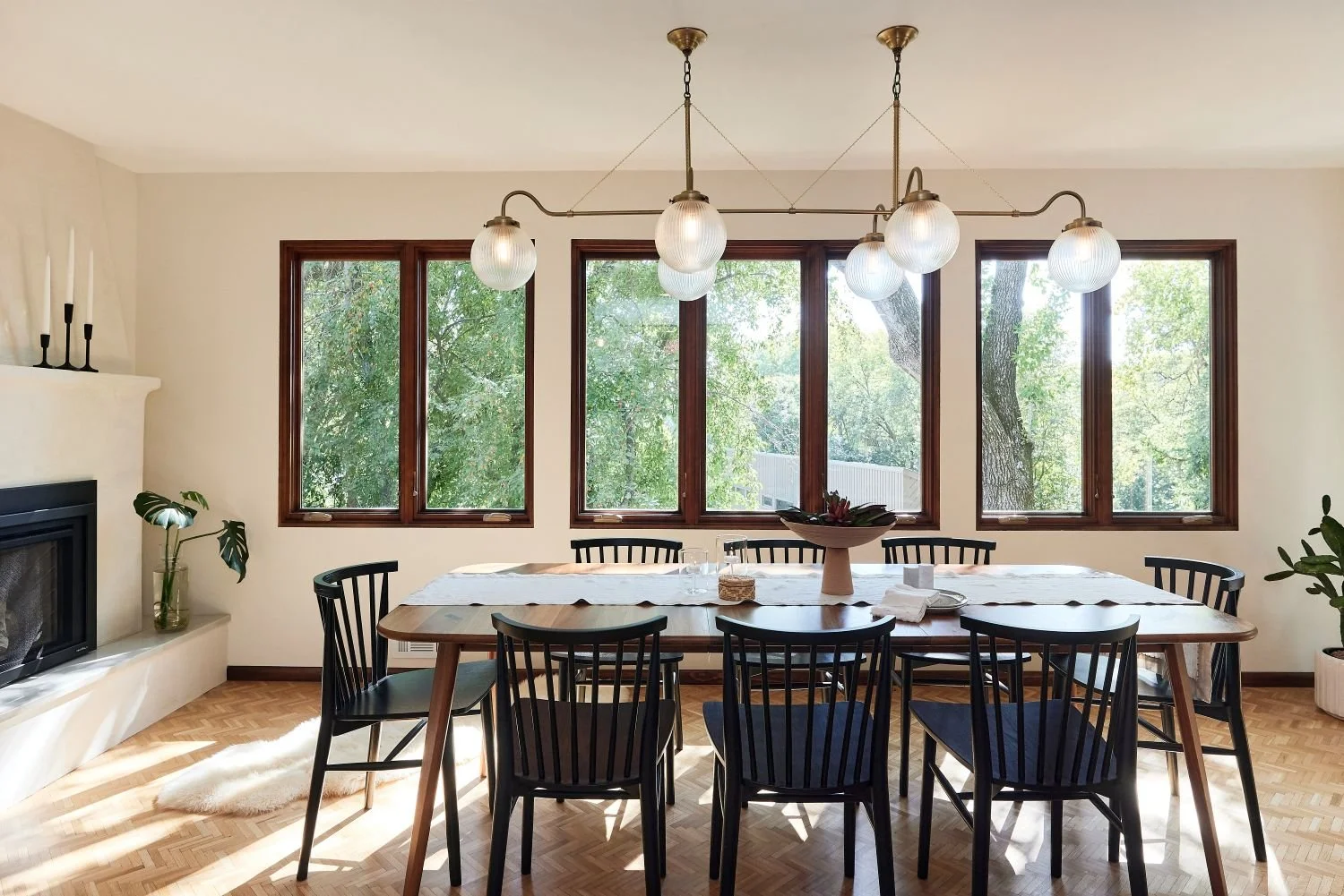 Golden Valley dining room, plaster custom fireplace, gas fireplace, black wood chairs, round glass ball shaped chandelier, terracotta plant, macrame wall hanging. 