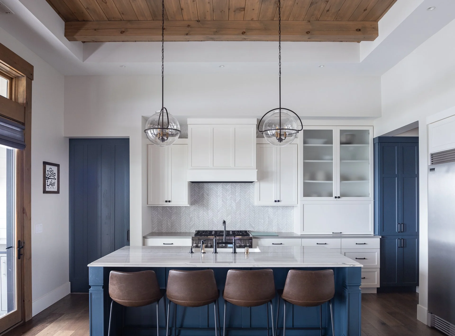 Custom white and navy kitchen cabinetry with large island, pendant lights, and wood beam ceiling