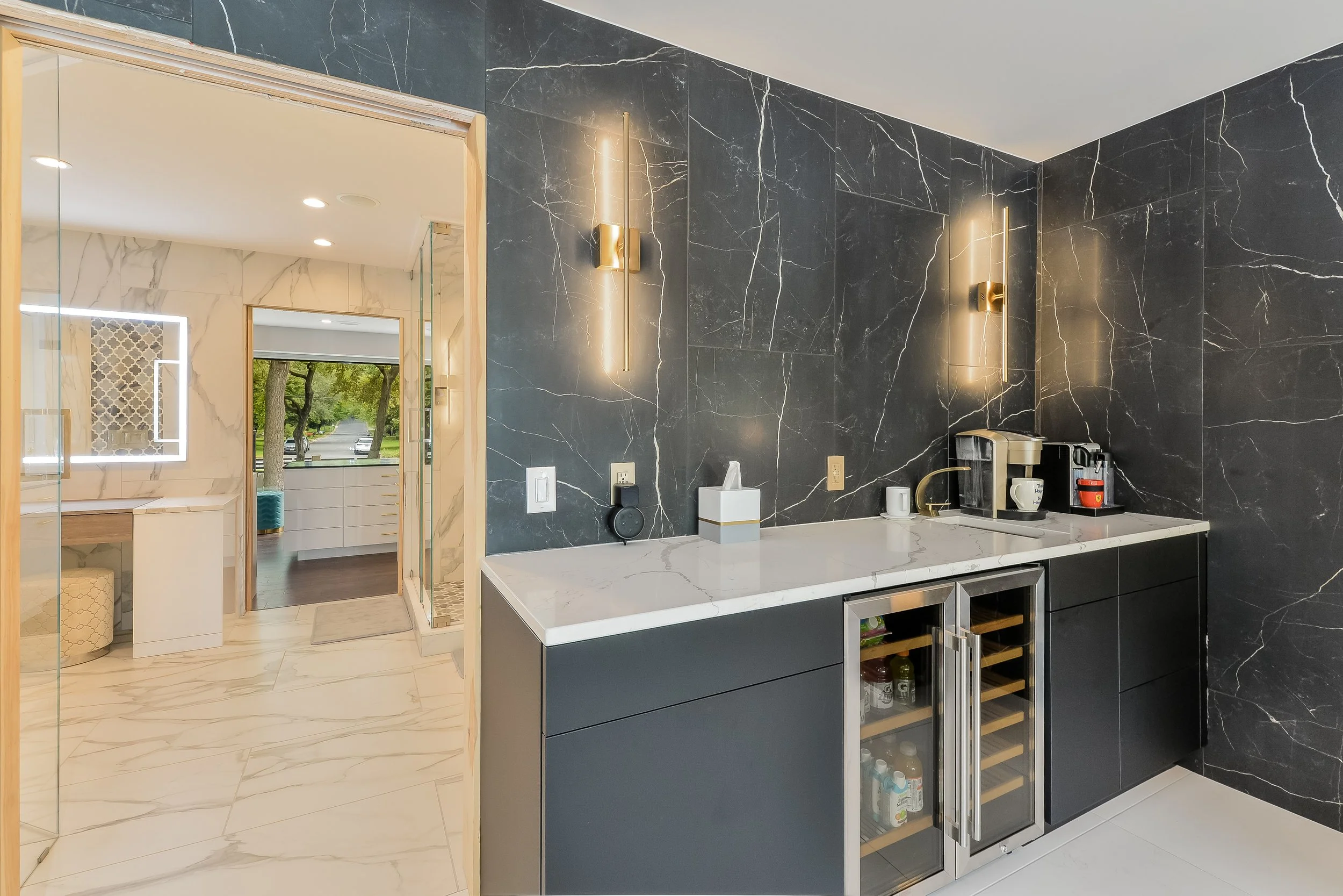 Custom dark coffee bar in primary suite with marble backsplash, beverage refrigerators, and brass lighting