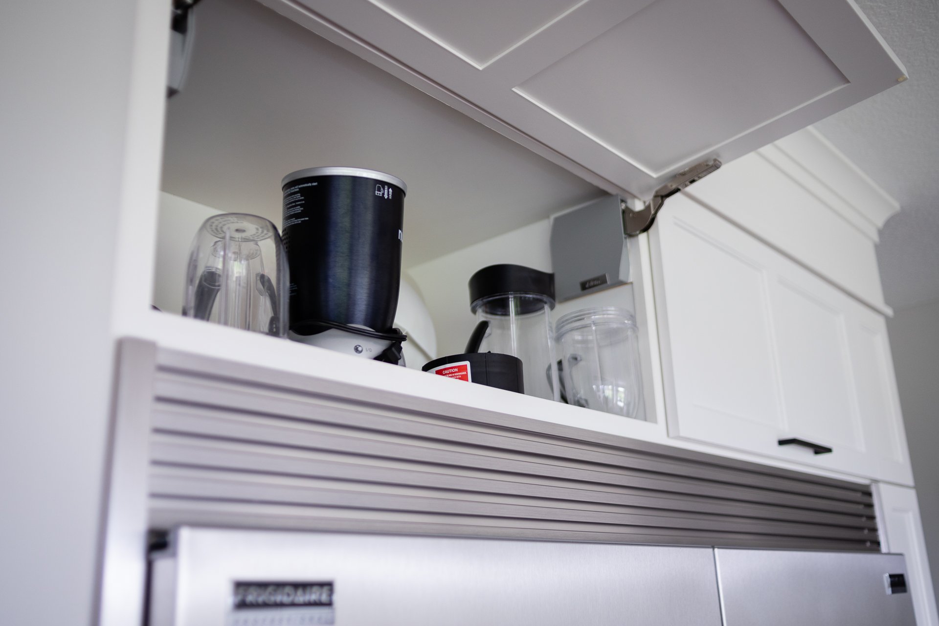 Lift-up upper cabinet with hidden appliance storage above refrigerator