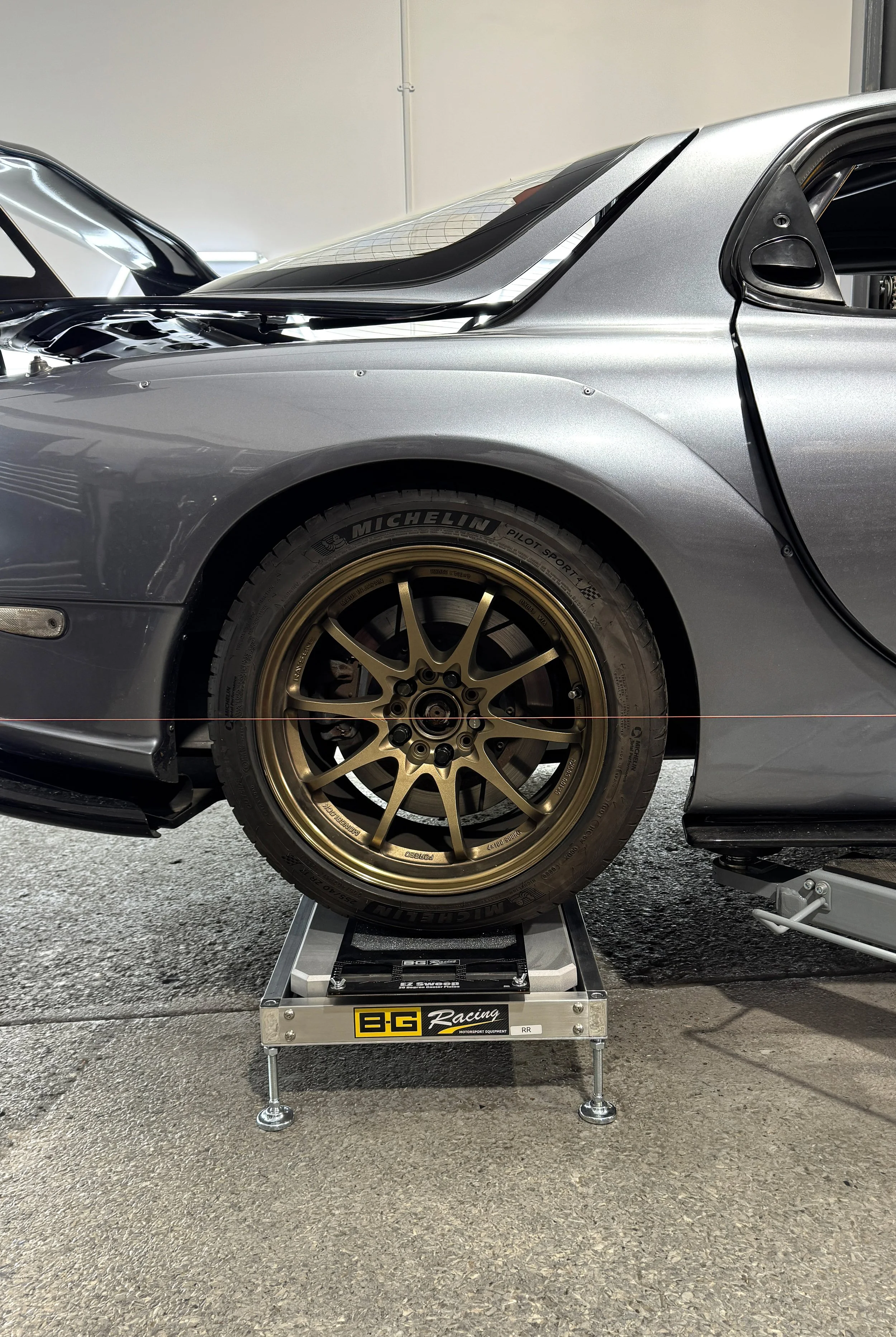 Mazda RX-7 track car on corner-weight scales and turn plates during a string alignment setup