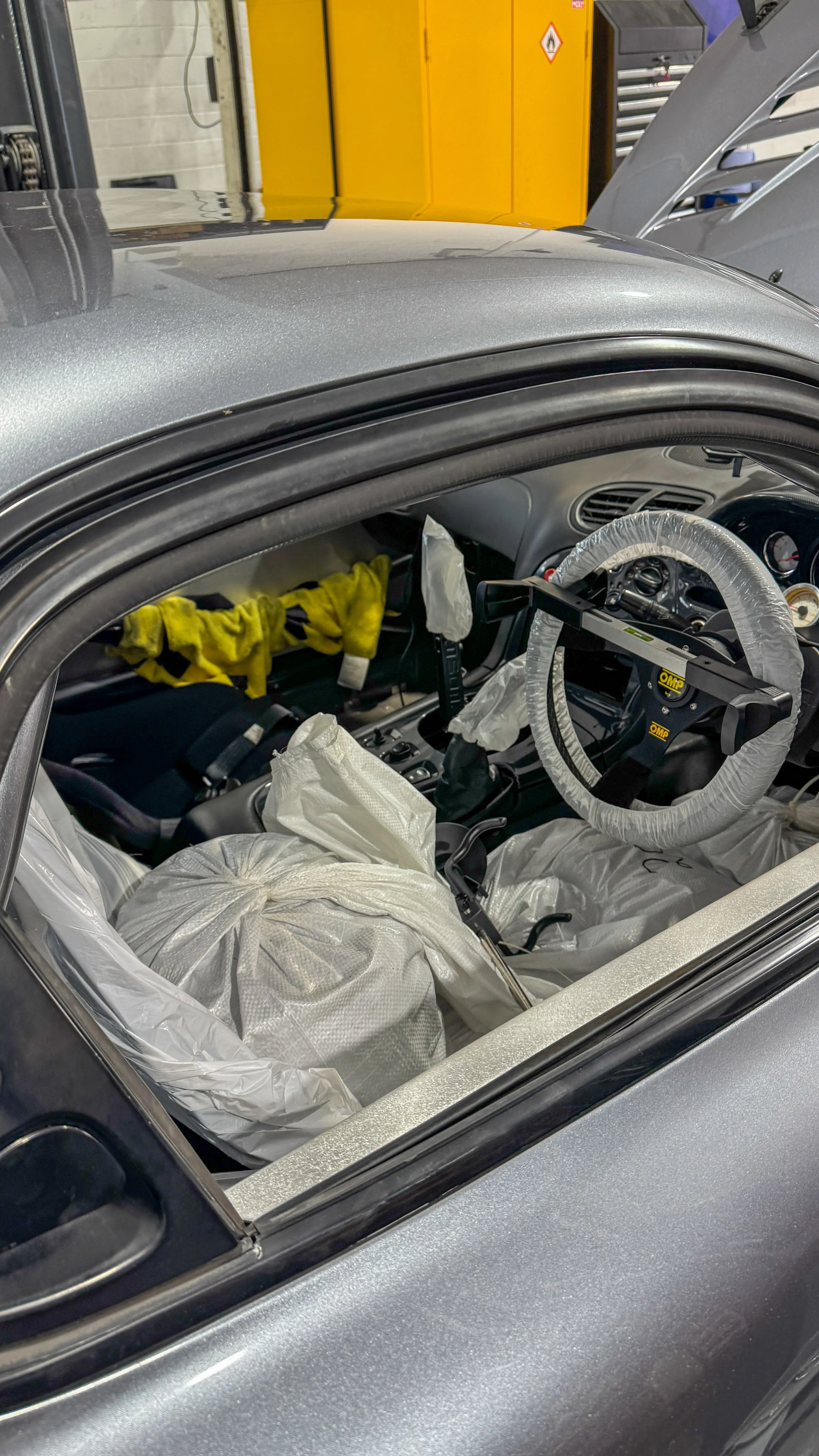 Mazda RX-7 track car interior prepared for geometry setup with protective covers, driver ballast and steering wheel centring equipment