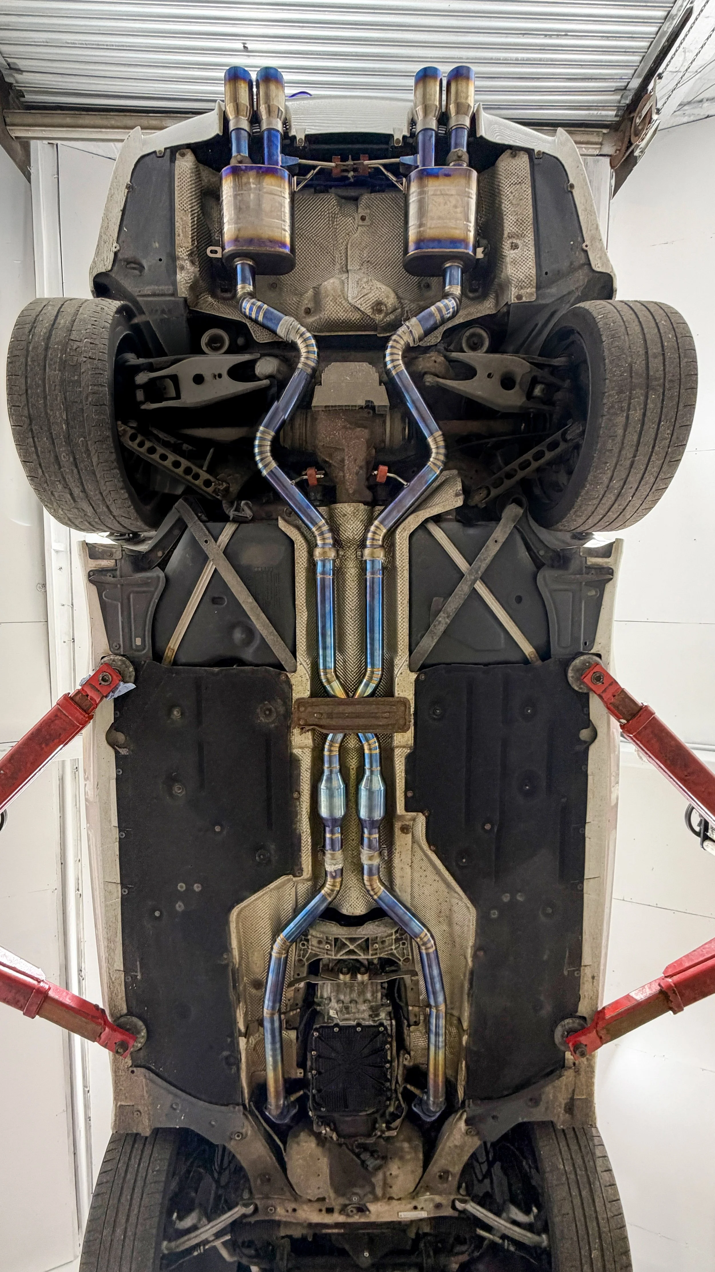 BMW E92 track car underbody inspection on a workshop ramp with titanium quad-exit exhaust system