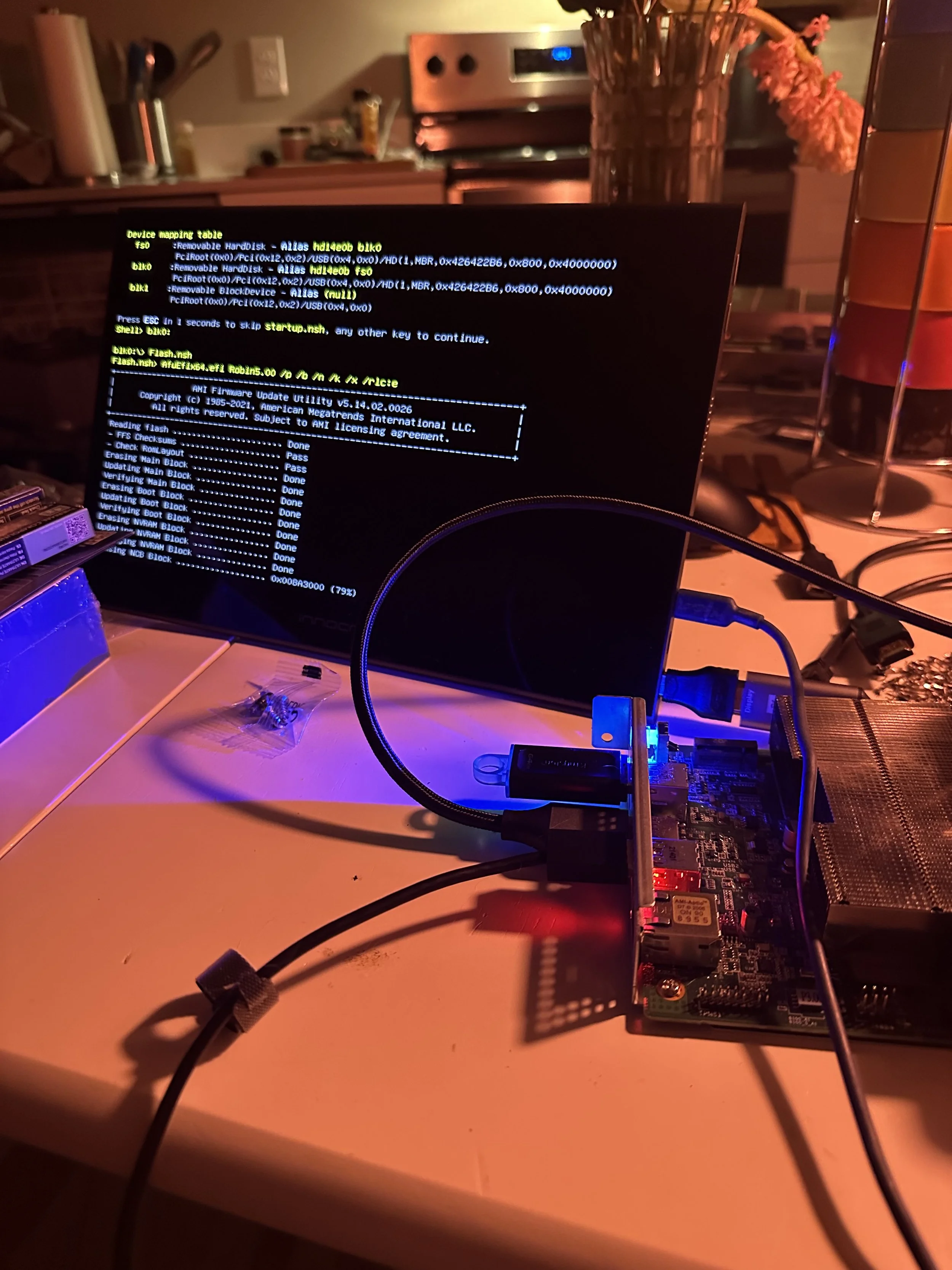 A computer monitor displaying a BIOS screen with text and commands related to firmware updates and hardware configuration, placed on a desk with various computer components and cables nearby.